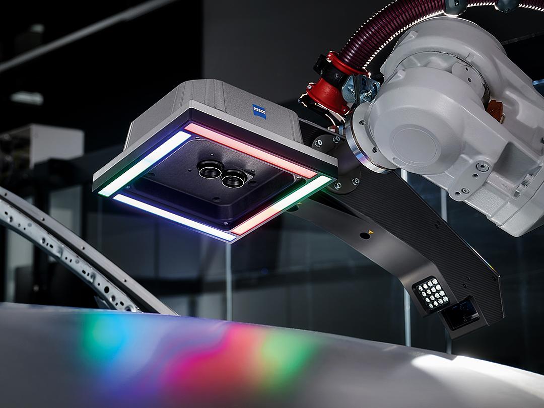 Un bras robotisé équipé d'un capteur de numérisation 3D ZEISS survole une surface métallique, éclairée par des lumières LED multicolores.