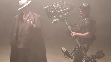 A camera operator films a man dressed in vintage attire on a foggy set using professional cinema equipment, showcasing ZEISS lens technology in a production environment.