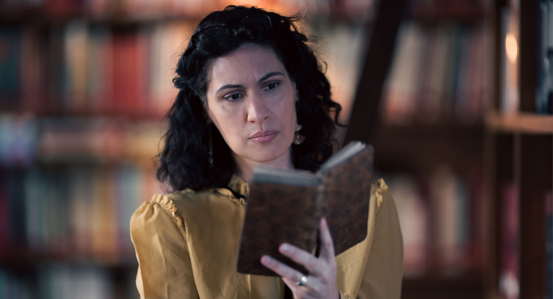 A woman stands in a historic library filled with bookshelves and long wooden tables covered in documents, viewed through a ZEISS lens.