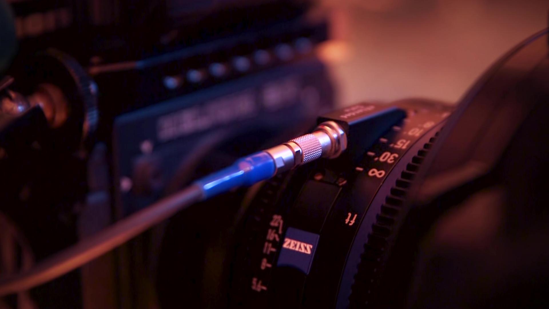 Close-up of a professional camera setup featuring a ZEISS cine lens with a connected control cable.