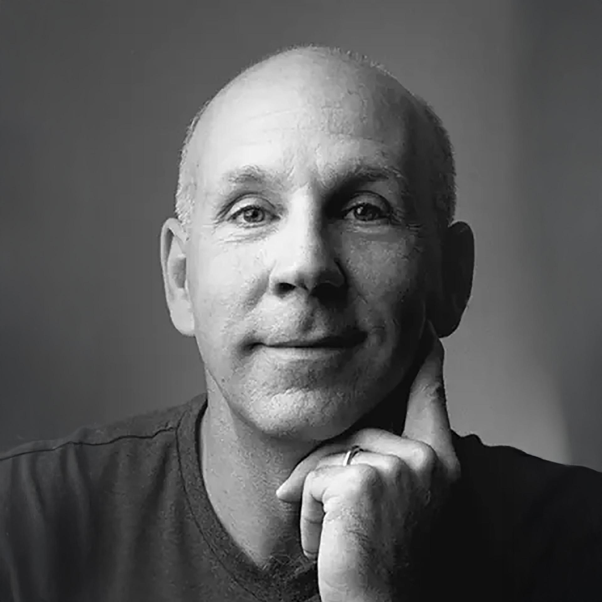 A man is operating a professional video camera with a mounted microphone on a tripod in an outdoor field.