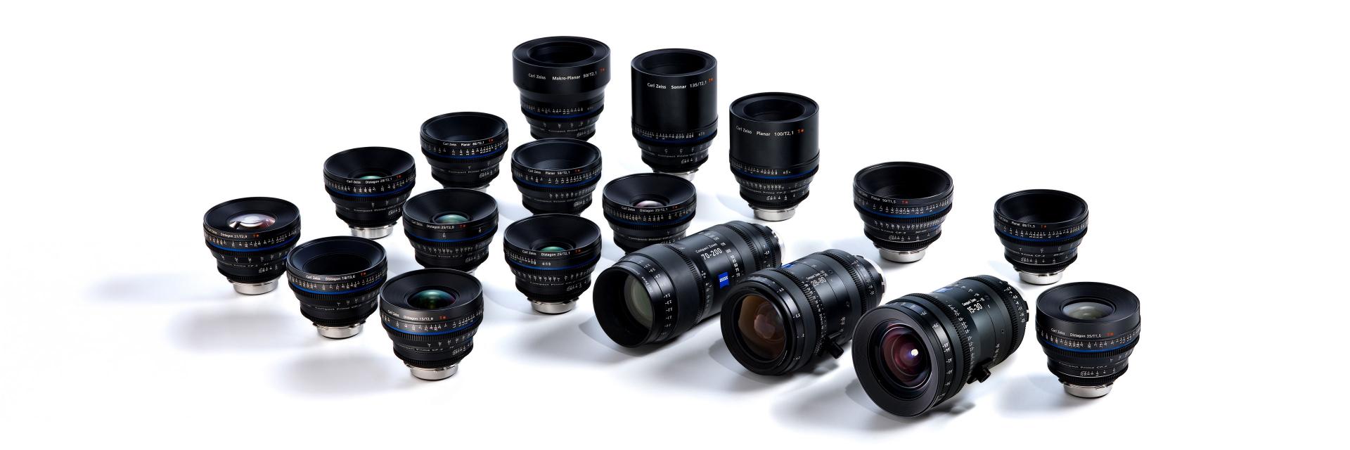 Eighteen professional ZEISS camera lenses are arranged on a white background, showcasing their detailed markings and glass elements.