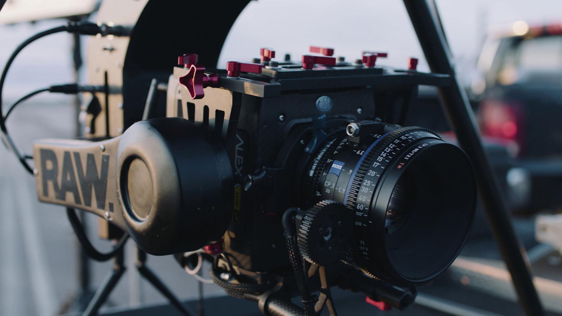 A professional cinema camera rig is equipped with a ZEISS lens and mounted on a support system outdoors.
