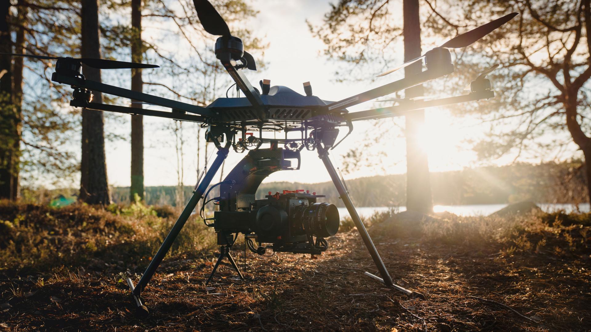 A professional drone equipped with ZEISS camera technology stands on a forest path at sunset.
