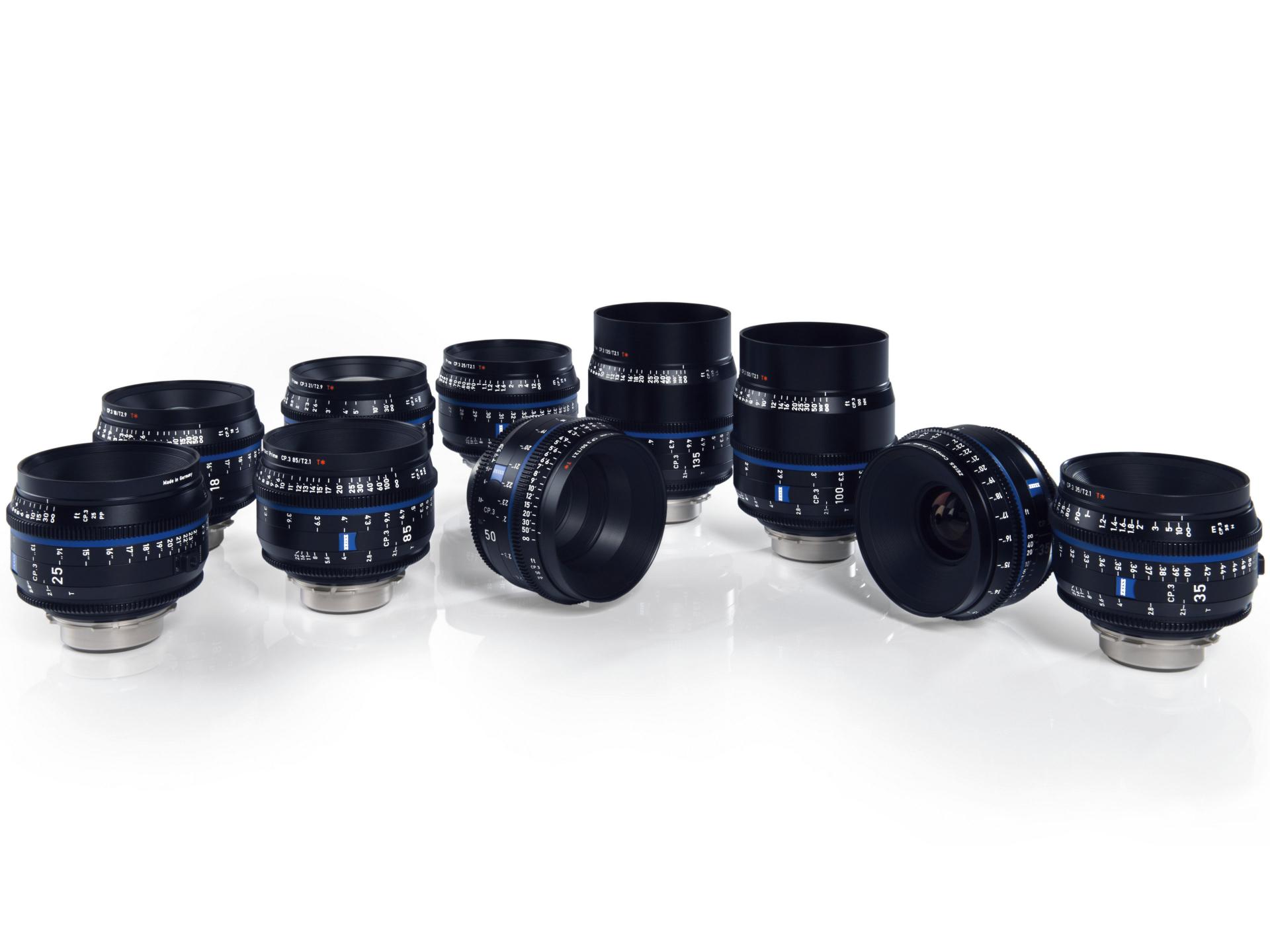 A set of ten ZEISS camera lenses with focus and aperture markings arranged on a reflective white surface.
