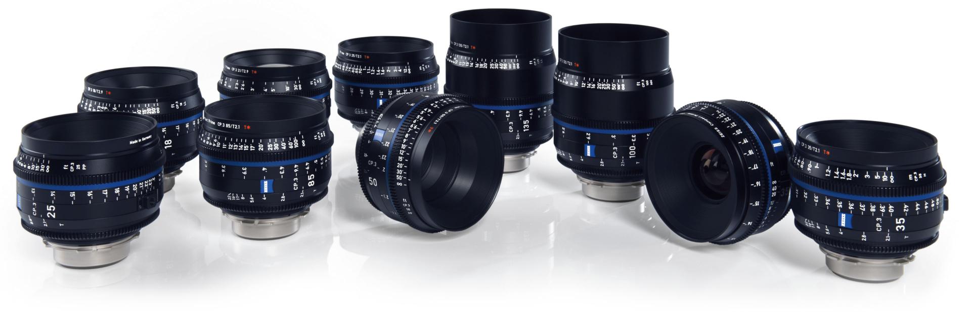 A set of ten ZEISS camera lenses with focus and aperture markings arranged on a reflective white surface.