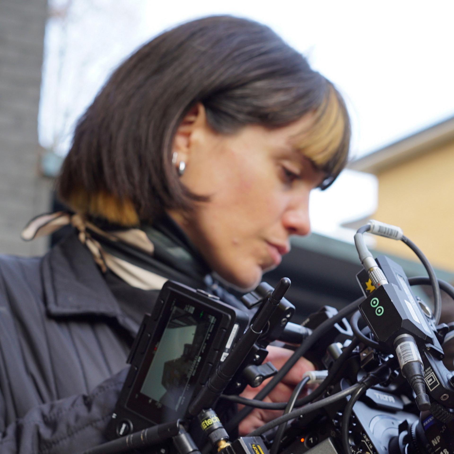 A woman is closely examining a professional camera rig equipped with multiple components and ZEISS lenses.