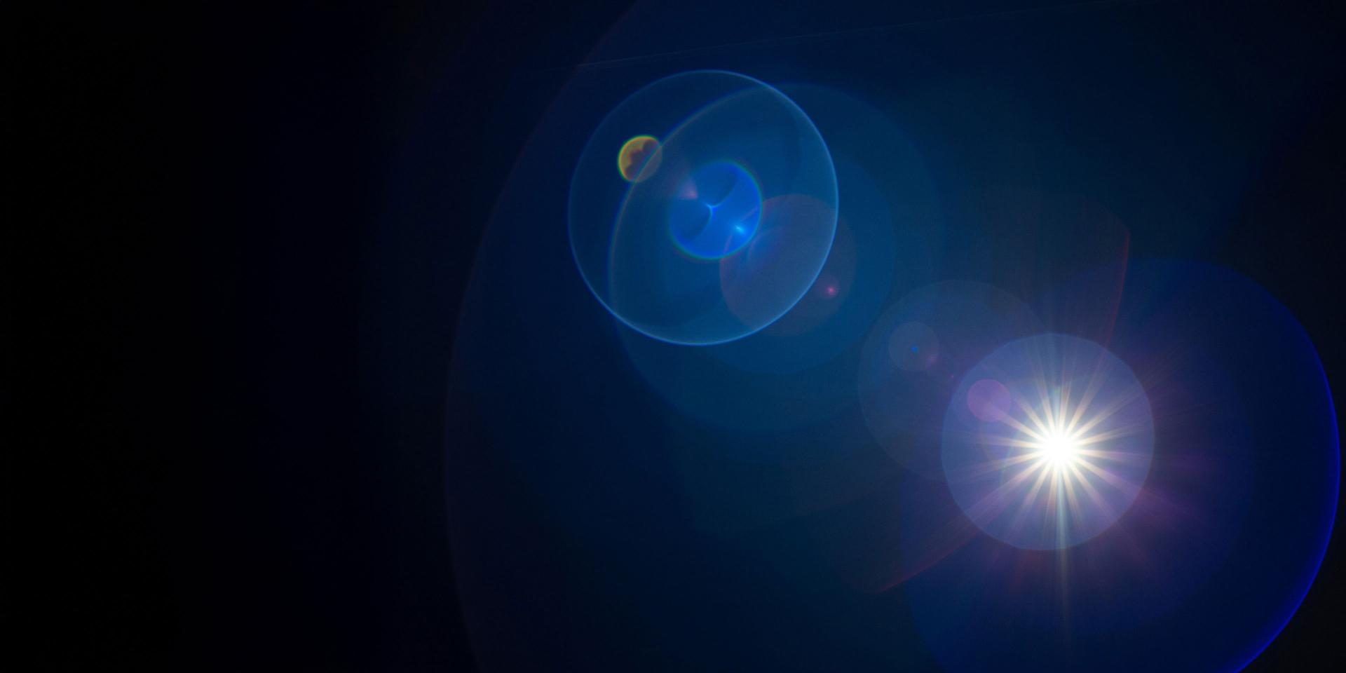 Bright lens flare with blue and purple light reflections against a dark background, illustrating ZEISS optical precision.