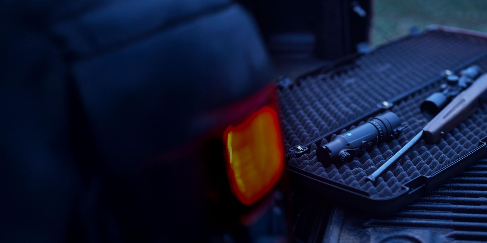 A ZEISS riflescope and accessories are displayed inside a protective foam case on the open tailgate of a vehicle.