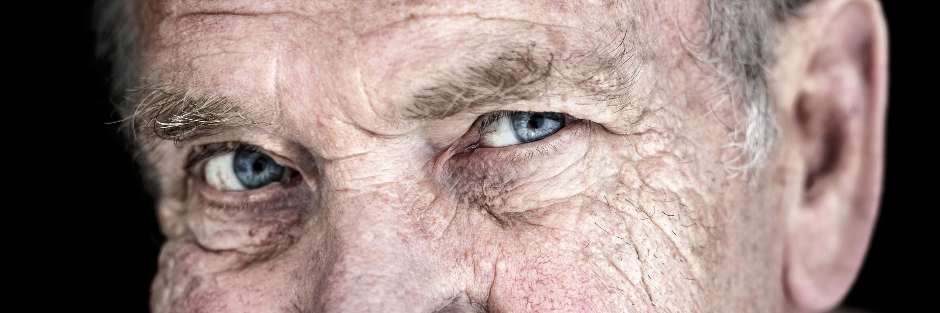 Close-up of an elderly man's face showing detailed features and bright blue eyes, with sharp focus highlighting skin texture, ideal for showcasing ZEISS optical precision.
