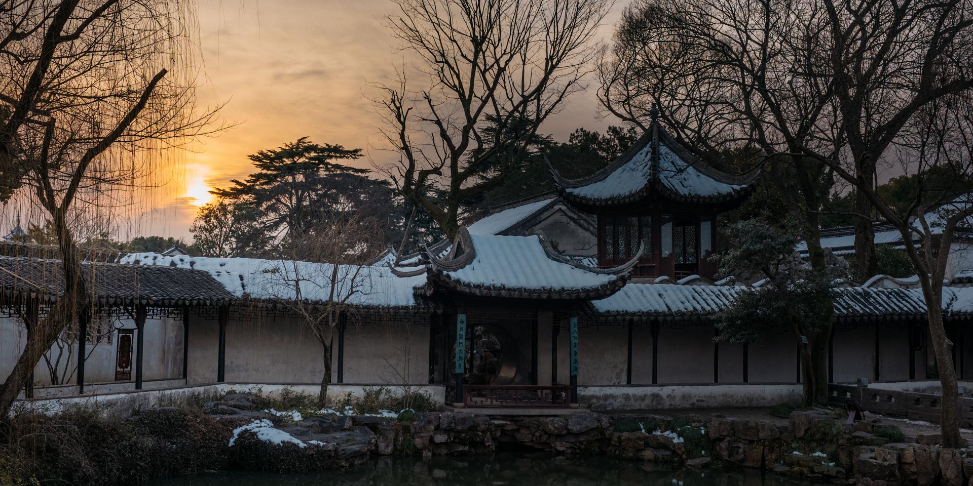 The image shows a serene scene of a traditional Chinese garden during a snowy sunset. 