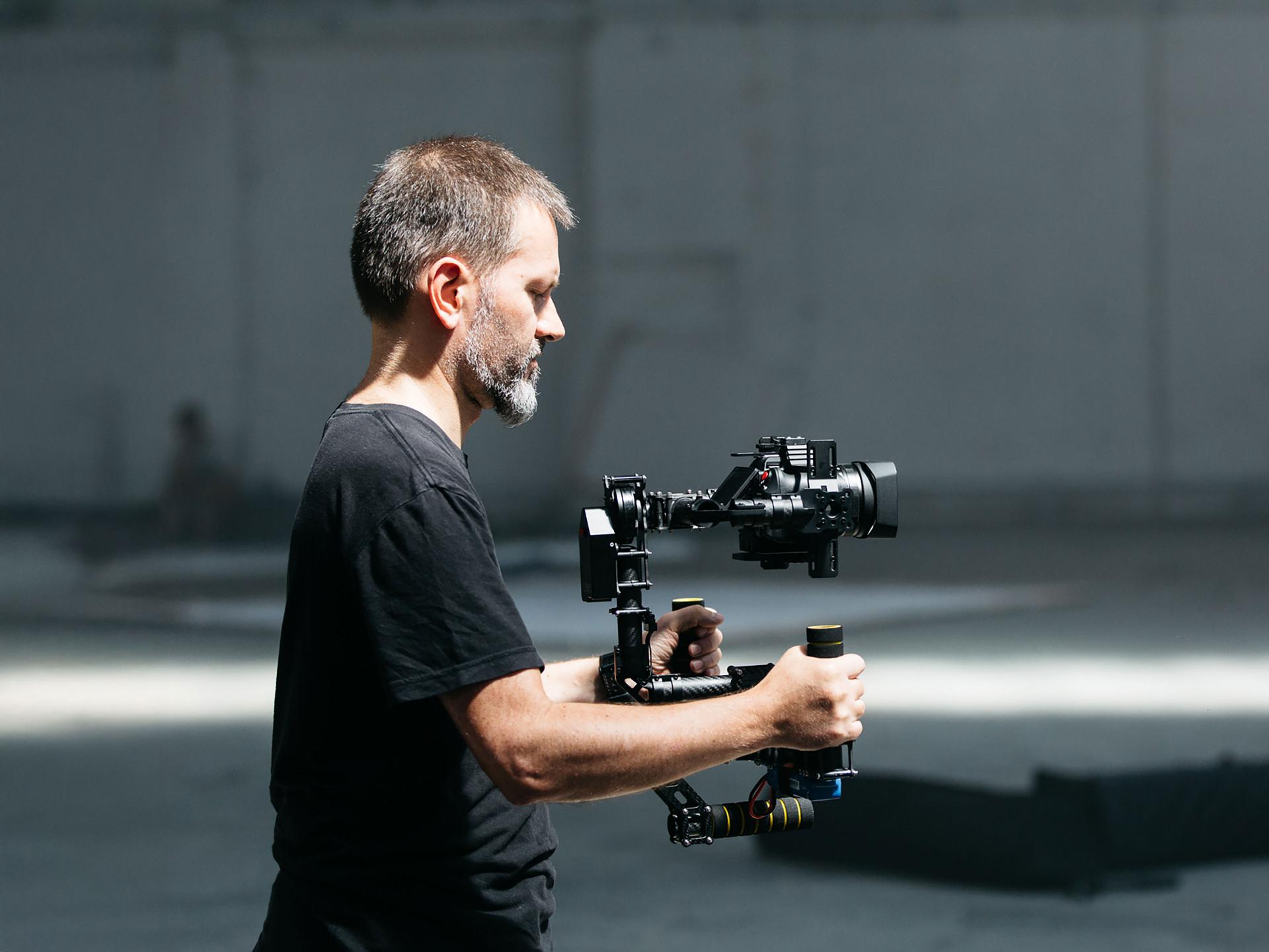 Man operating a professional camera mounted on a stabilizer rig in a well-lit indoor setting using ZEISS equipment.