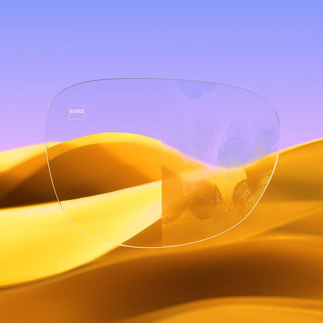 Image fractionnée d’un verre d’un côté transparent et propre, muni de ZEISS DuraVision Gold UV, et de l’autre côté couvert de traces de doigt.