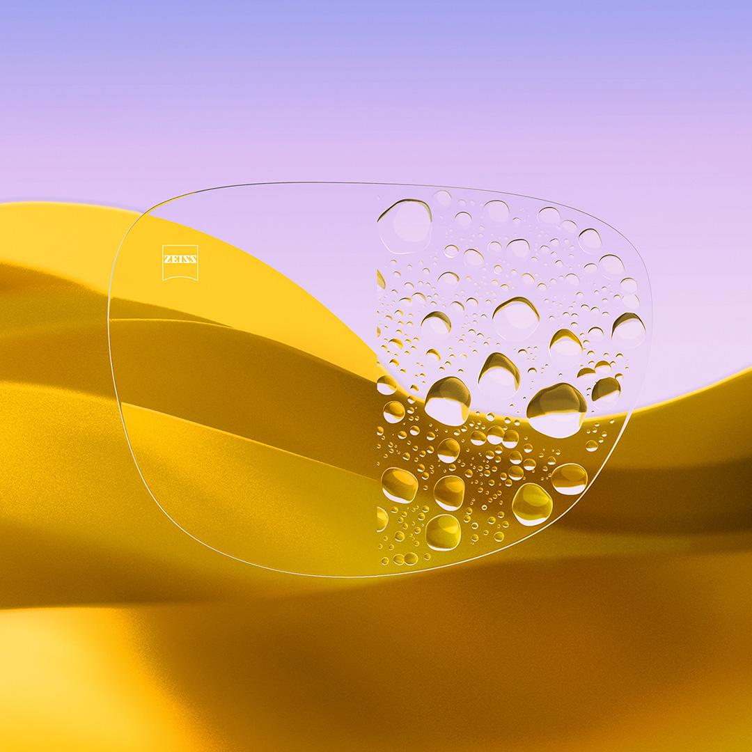 Image fractionnée d’un verre, d’un côté transparent et propre, muni de ZEISS DuraVision Gold UV, et de l’autre côté couvert de gouttes d’eau.