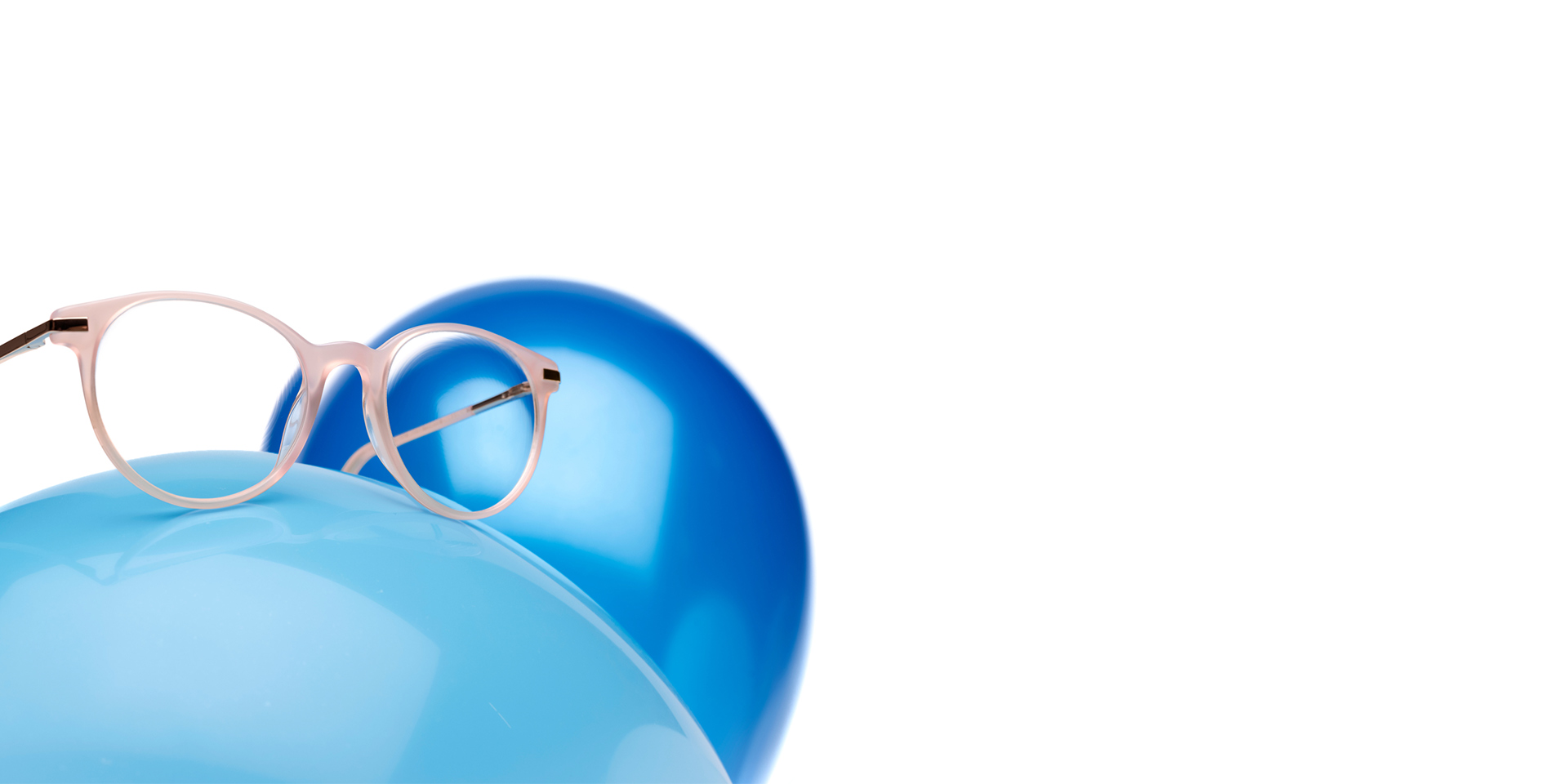 Des verres ZEISS MyoCare dans une monture beige rosé sont présentées sur un ballon bleu clair. Un autre ballon bleu légèrement plus foncé est visible en arrière-plan.