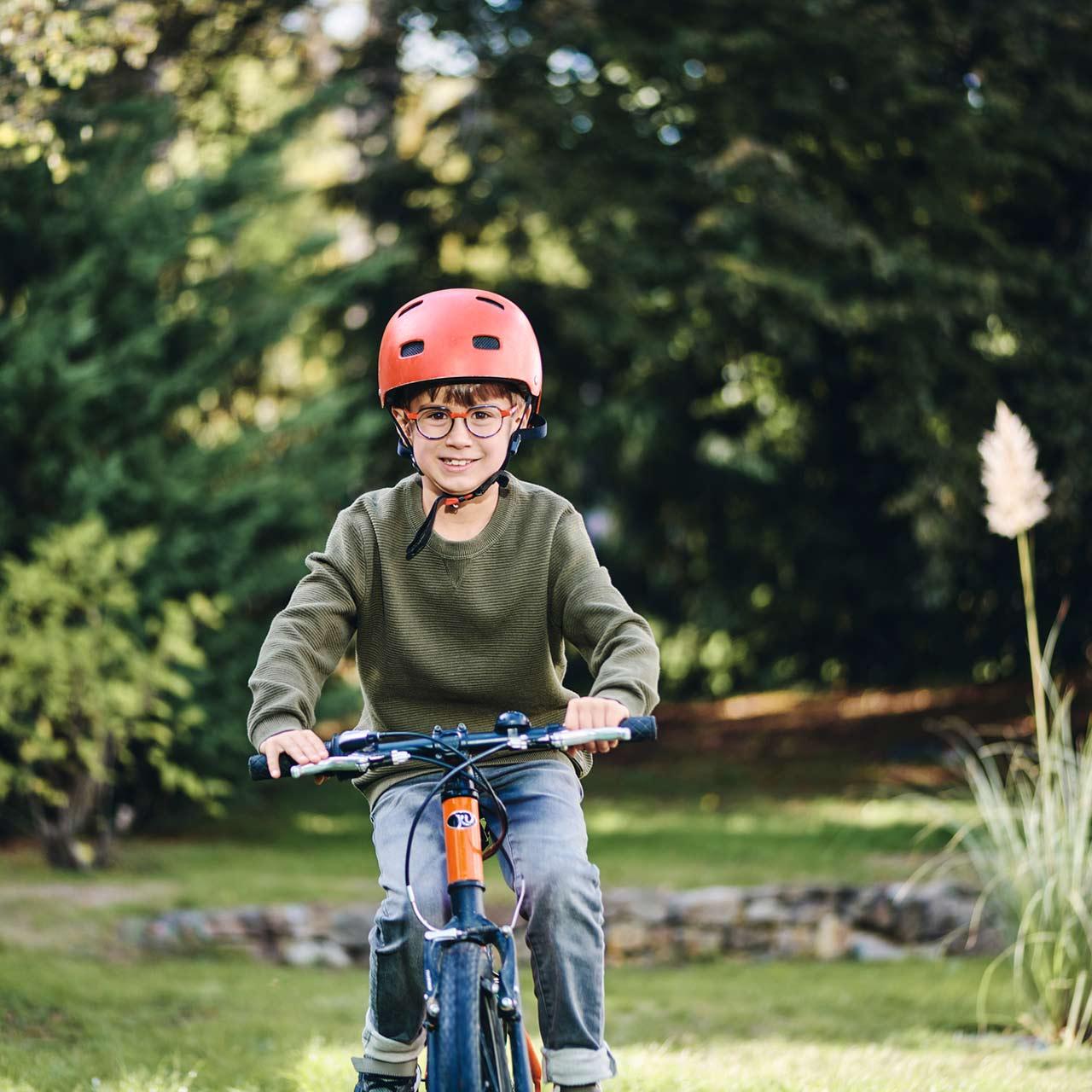 Garçon à lunettes faisant du vélo en plein air et souriant