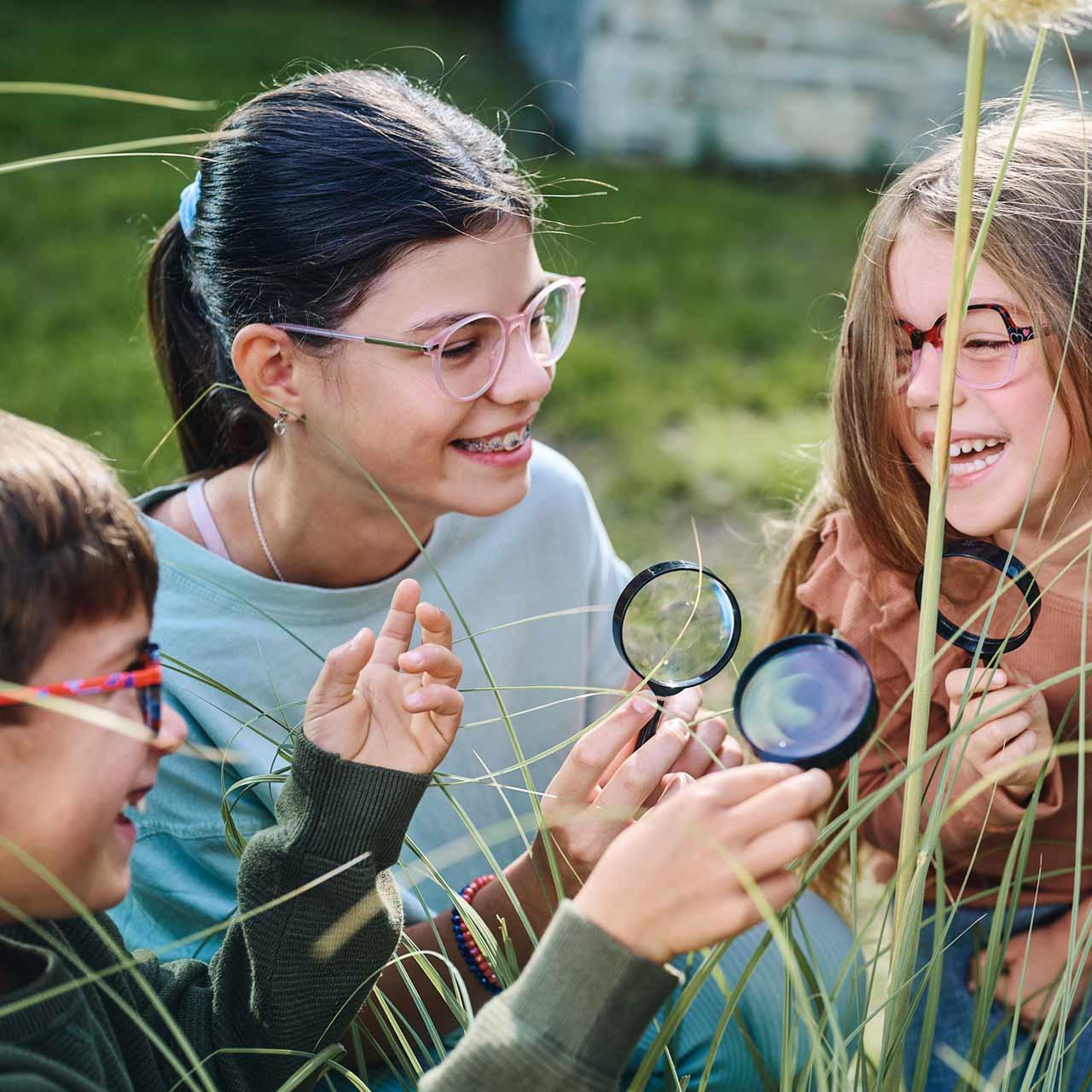 Groupe d’enfants avec des lunettes et des loupes jouant et riant à l’extérieur