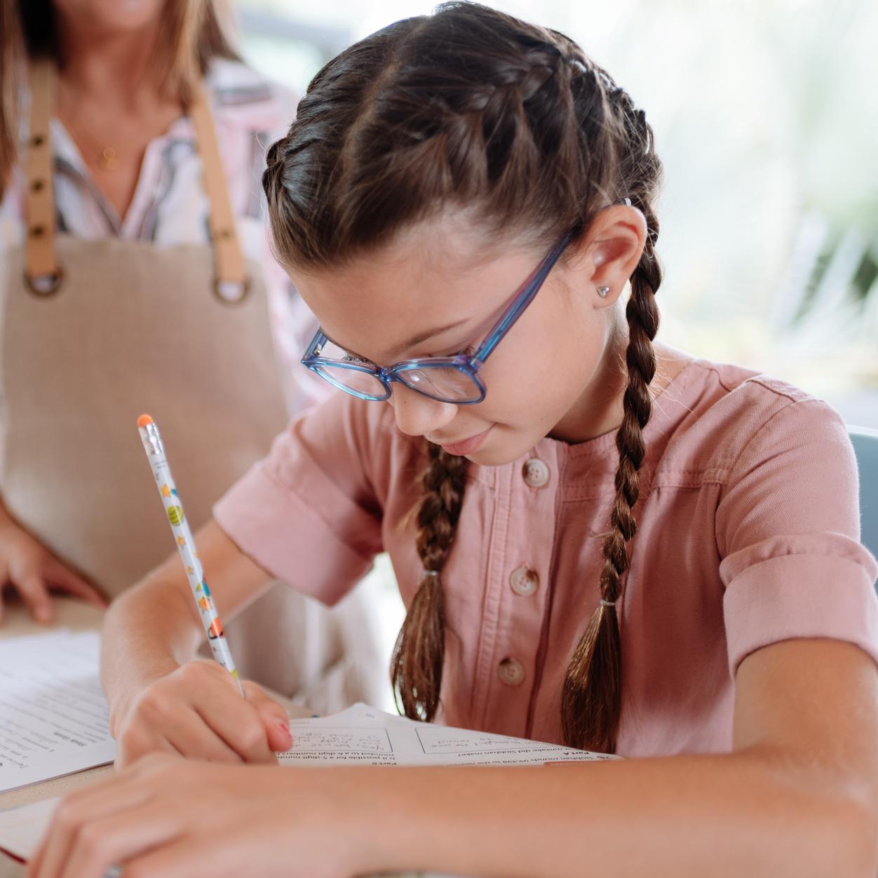 Une jeune fille portant des lunettes écrit au stylo