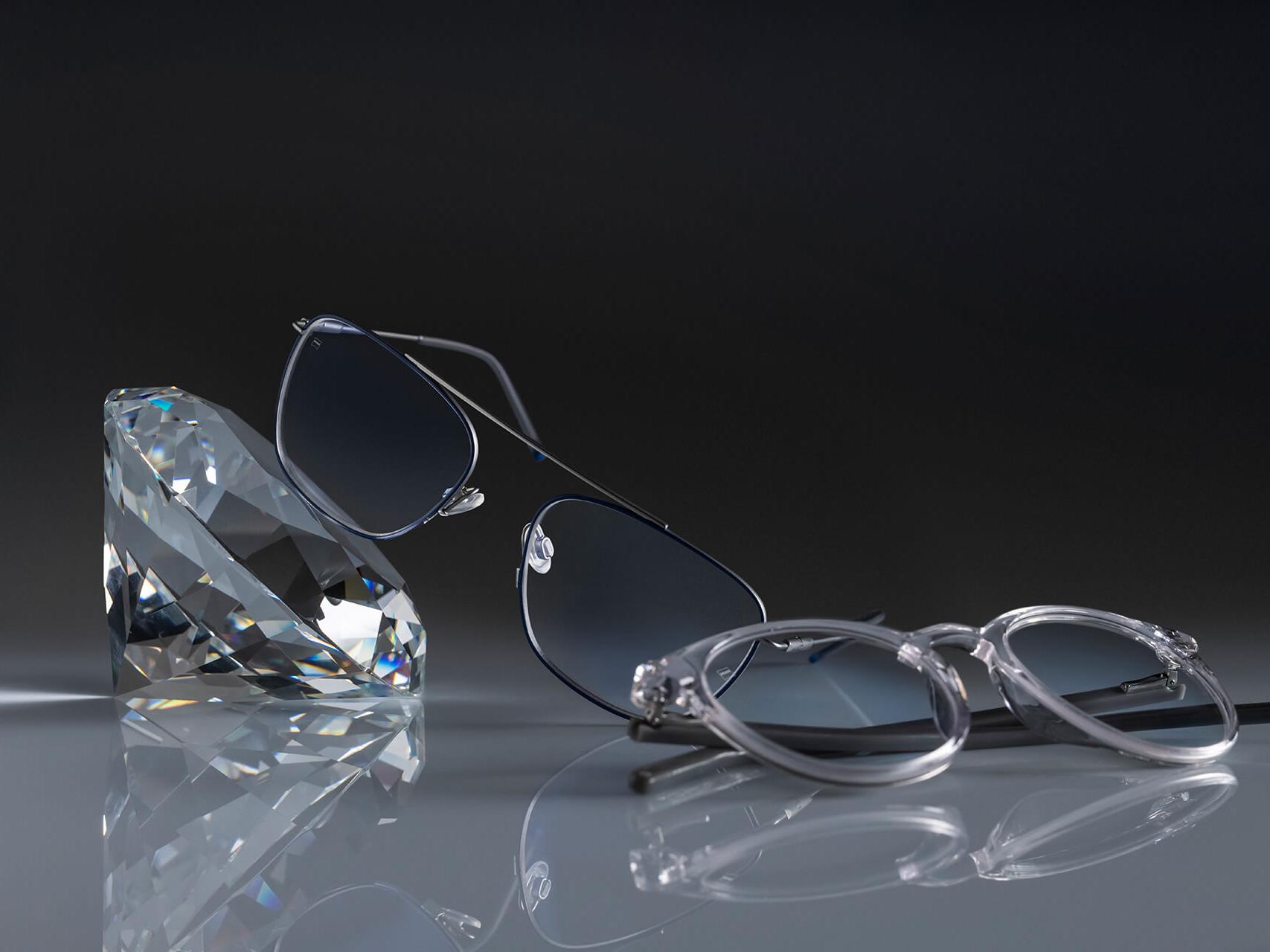 Deux paires de lunettes avec des verres ZEISS dotés du traitement ZEISS le plus résistant jamais réalisé – DuraVision® Platinum. Une paire de lunettes est appuyée contre un cristal, l’autre est posée à plat sur le sol. Tous deux disposent de verres transparents sans reflets bleutés.