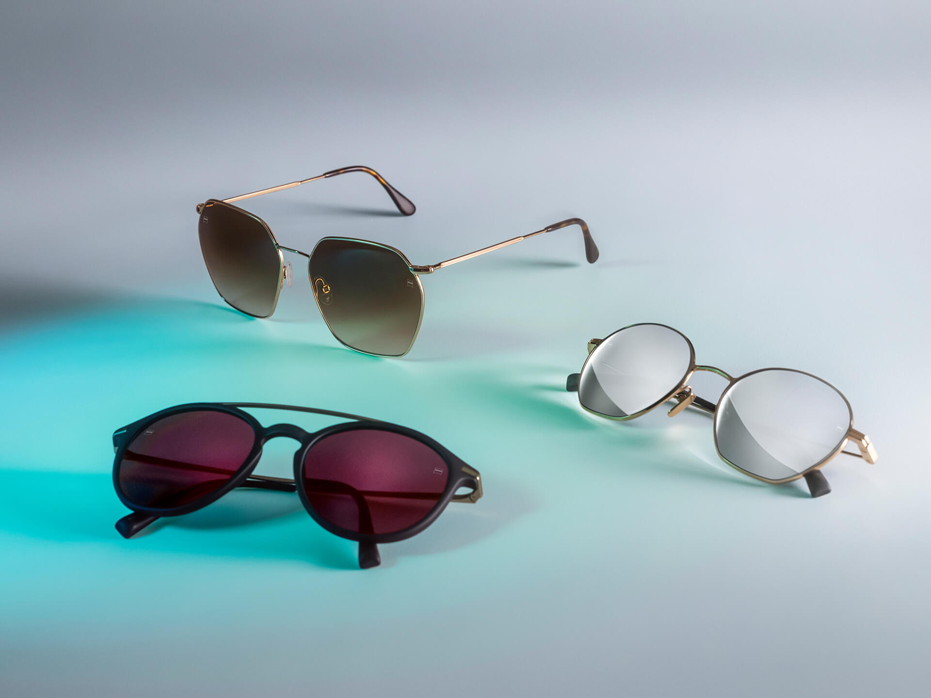 Trois paires de lunettes de soleil avec des verres solaires ZEISS de différentes couleurs, dotés des traitements DuraVision Sun, DuraVision Mirror et Flash Mirror, visibles sur un arrière-plan blanc avec un reflet de lumière bleue.
