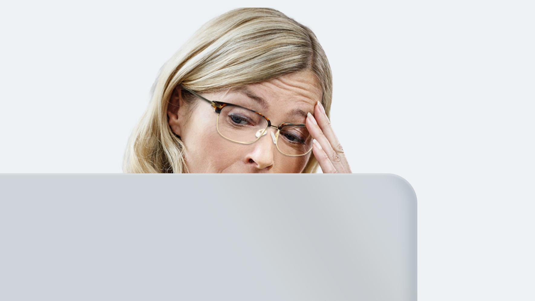 Une femme d’âge moyen aux longs cheveux blonds porte des lunettes pour la vue de loin. Elle souffre de fatigue oculaire, parce que ses verres ne sont pas faits pour fixer un écran toute la journée.