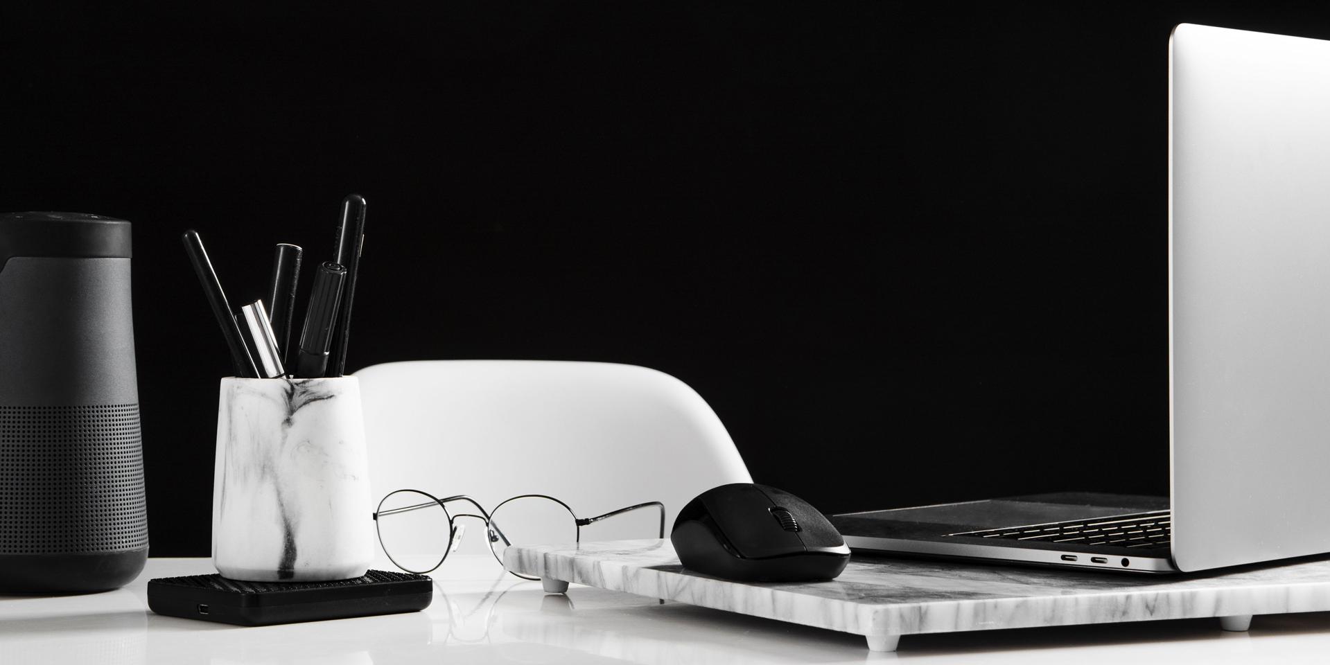 Poste de travail bien ordonné avec un ordinateur portable ouvert et une souris sur le côté droit. Une paire de lunettes est posée devant. Une boîte avec des stylos se trouve à gauche de l’image.