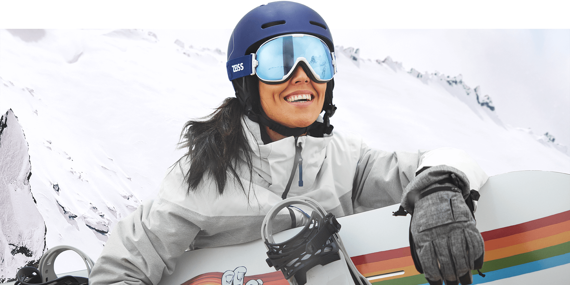 Une jeune femme portant des lunettes de neige dotées de la technologie interchangeable de ZEISS et tenant un snowboard.