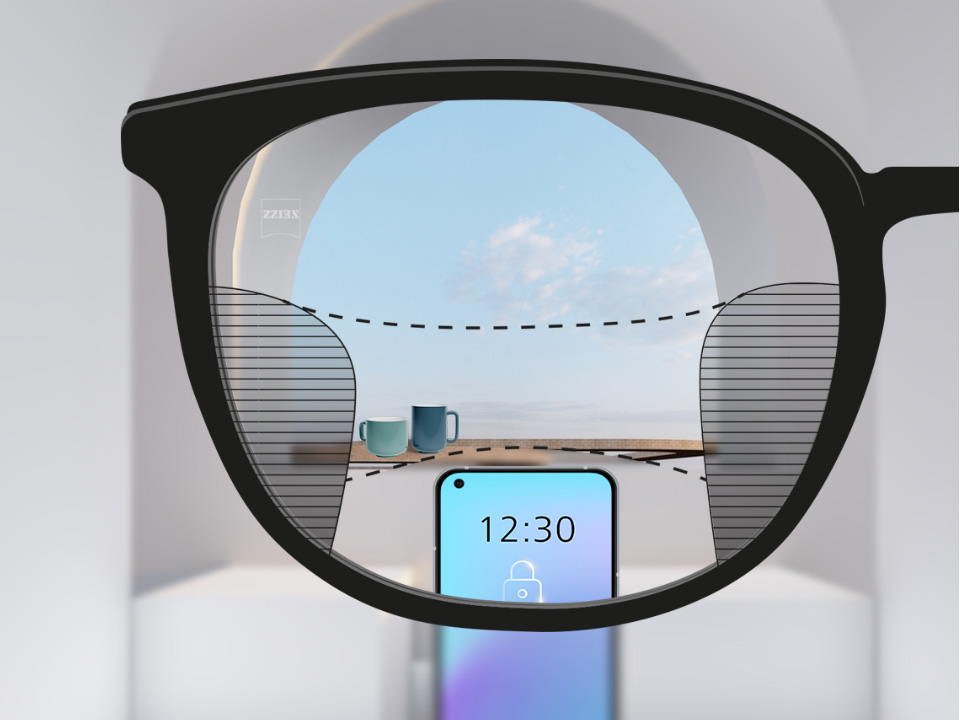 Image montrant à travers un verre ZEISS SmartLife progressif un point de vue sur un téléphone et des tasses en arrière-plan, la vision étant parfaitement claire, hormis une fine zone floue à droite et à gauche.
